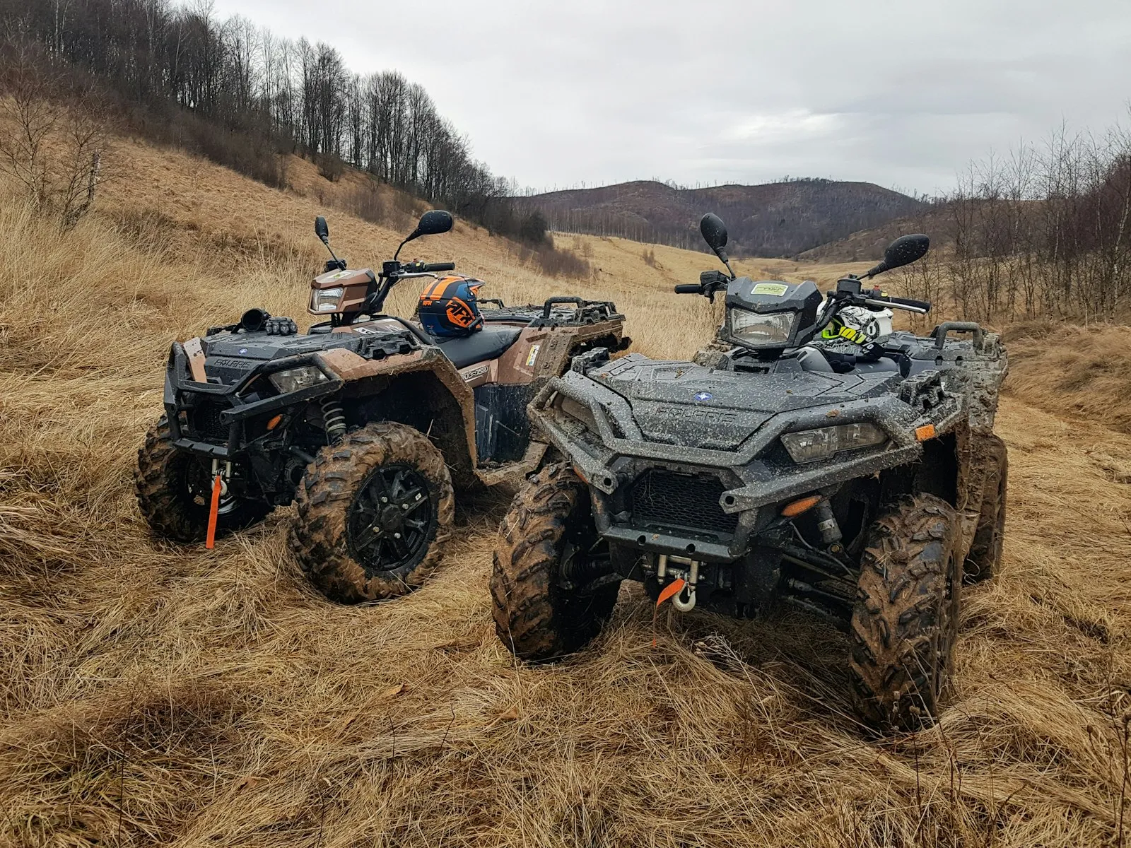 Two muddy ATVs parked on a grassy hillside