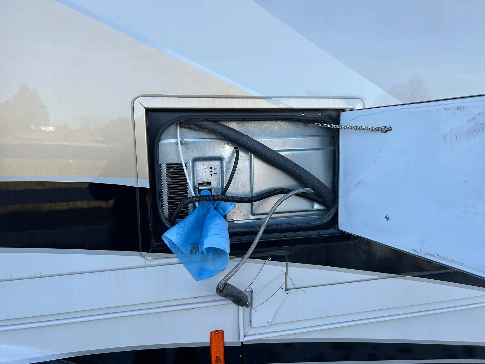 The refrigerator’s exterior access panel open on the 2020 Tiffin Allegro Red 33AA, with the water line disconnected and a towel under the fitting